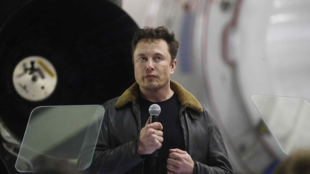 SpaceX CEO Elon Musk standing and holding a microphone.