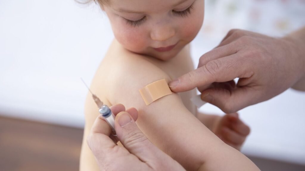A small person looks at the band-aid being applied to their arm.