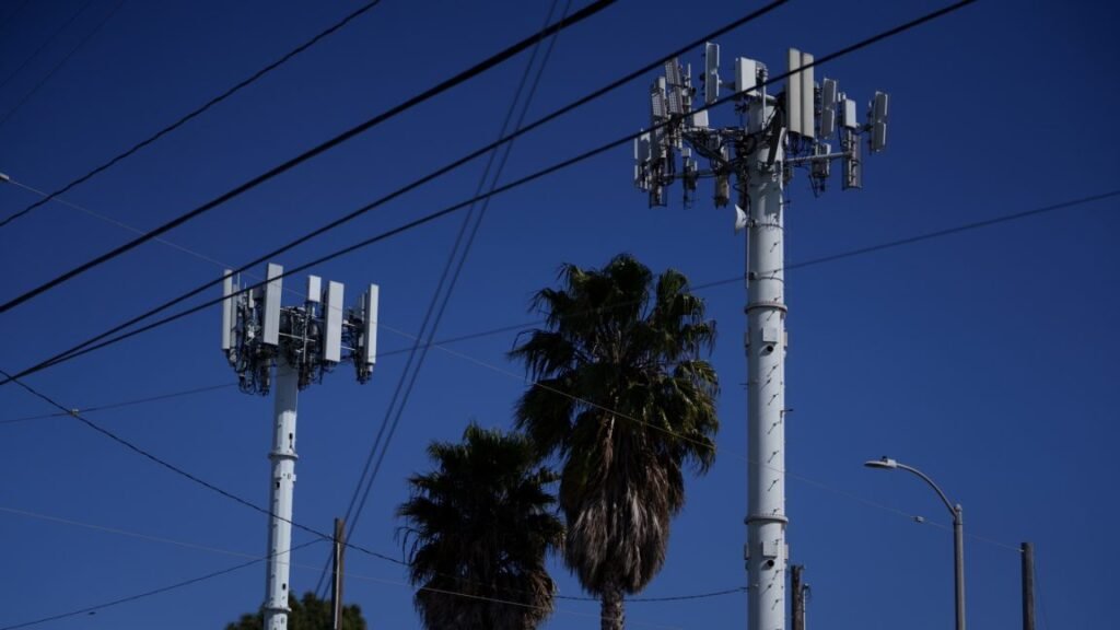 A picture of two cellular towers. Trees and aerial power lines are also in the photo.