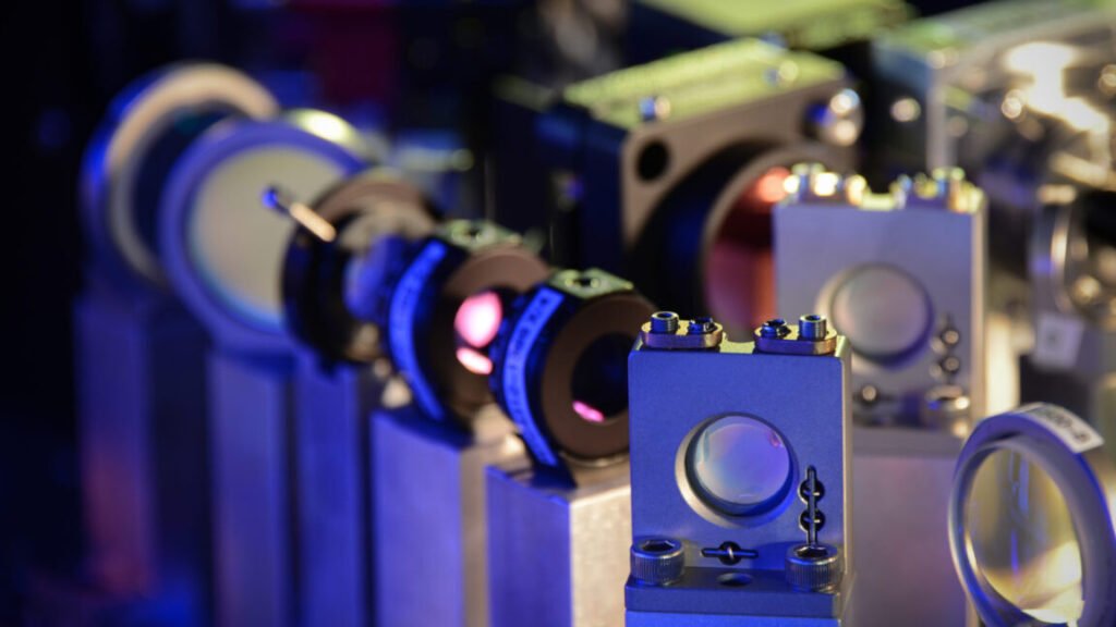 Image of a series of lenses held by vertical metal pillars. Other sets of lenses are behind these, and the background is black.