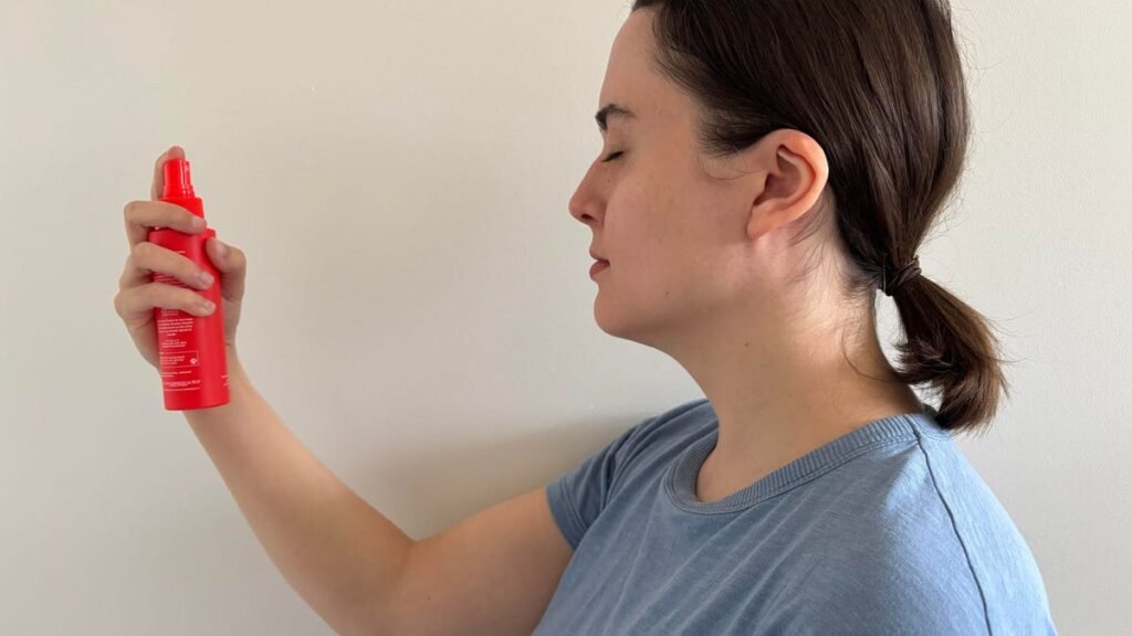The CNET reviewer using the Tower 28 SOS Rescue Spray while wearing a light blue tee in front of a white wall.