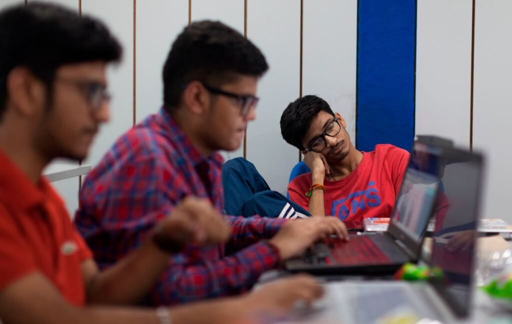 Figuring out why a nap might help people see things in new ways Image of two people typing at computers, with a third in the back dozing off with his head resting on his hand.
