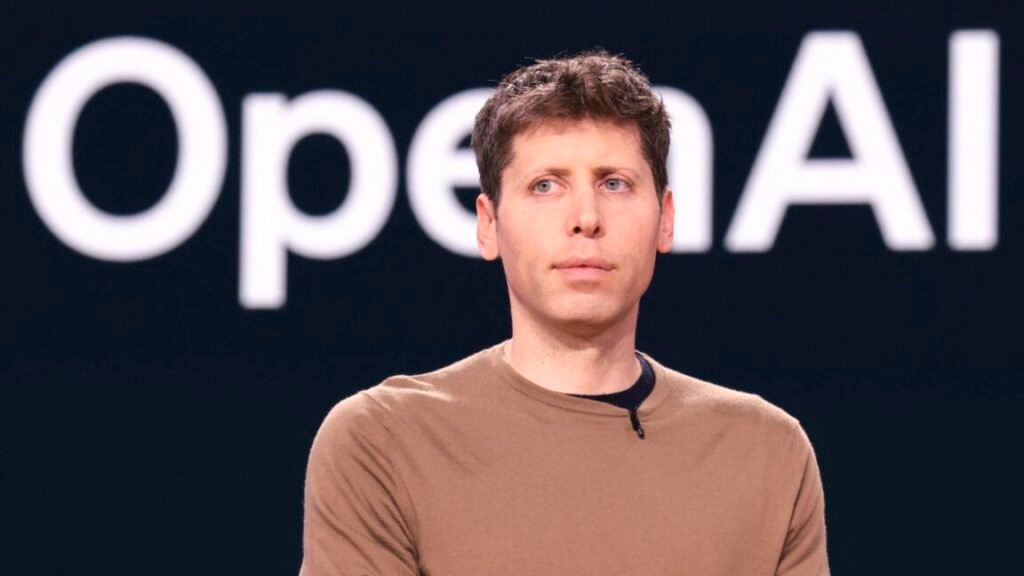 OpenAI CEO Sam Altman standing in front of a backup with a large OpenAI logo.